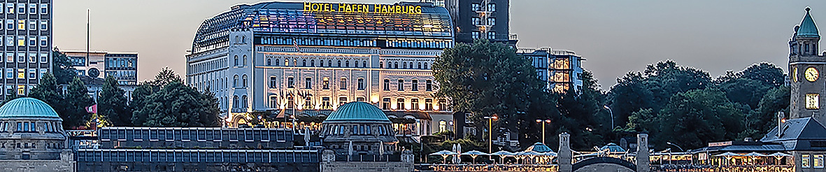 Blick auf die beleuchteten Landungsbrücken und das Hotel Hafen Hamburg in der Abendstimmung an der Elbe