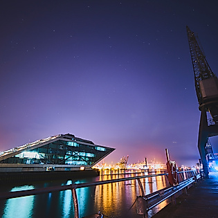 Dockland und Hafenkräne bei Nacht mit Lichtern und Spiegelungen auf der Elbe in maritimer Szenerie