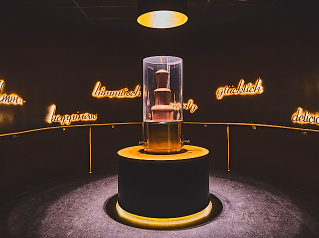 Beleuchteter Schokobrunnen im dunklen Ausstellungsraum des Chocoversums Hamburg, zentral in Szene gesetzt