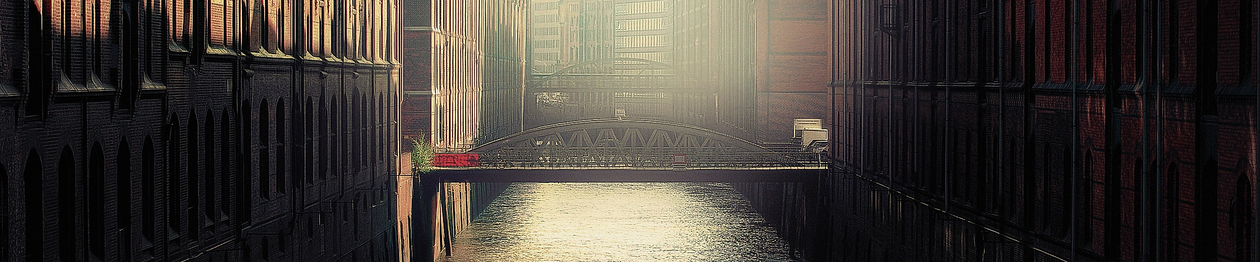 Schmale Wasserstraße der Speicherstadt im Gegenlicht mit reflektierendem Wasser und Backsteinfassaden
