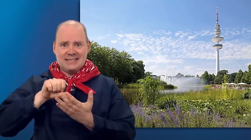 Mann gebärdet vor Hamburg-Kulisse mit Parklandschaft und Fernsehturm – barrierefreie Infos zu Grünflächen.