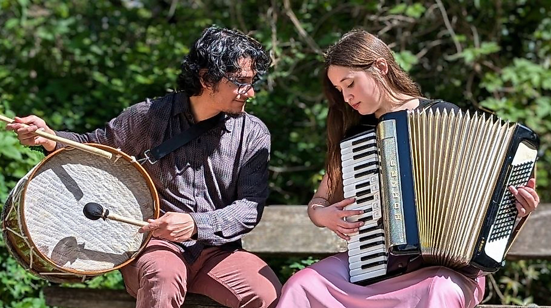 Víctor Gutiérrez und Isidora Caroca sitzen auf einer Bank. Während Víctor ein Schlaginstrument hält, hat Isidora ein Akkordeon.