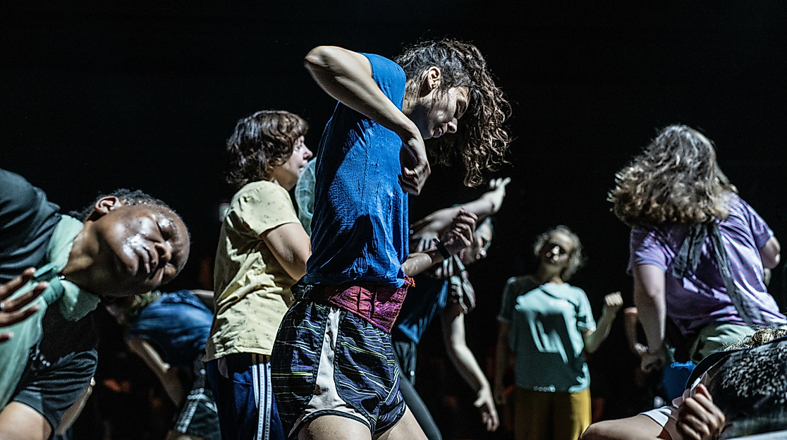 Dancers move intensely and expressively in a tight group formation on stage.