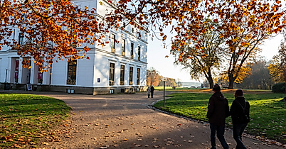 Spaziergänger:innen im herbstlichen Hirschpark Hamburg-Blankenese vor dem weißen Jenisch Hauss