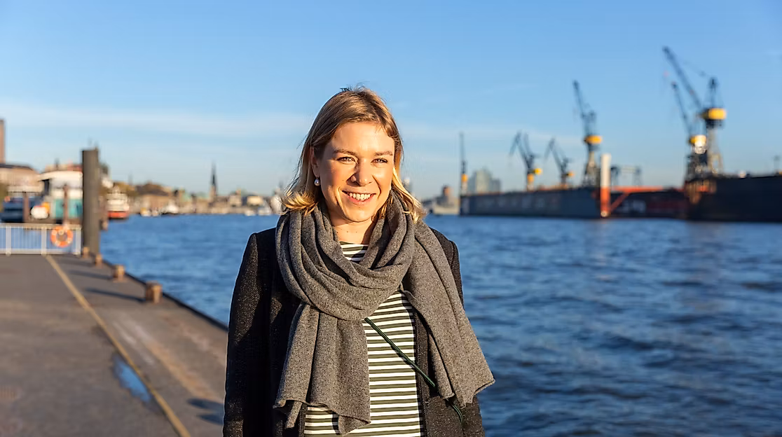 Frau am Hamburger Hafen bei Sonnenschein mit Blick auf die Elbe und Werftkräne im Hintergrund