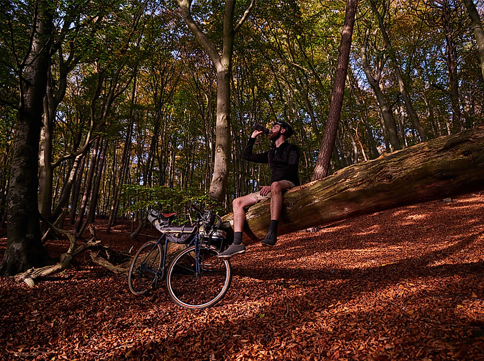 Radfahrer pausiert auf Baumstamm im herbstlichen Wald und genießt die Natur bei Sonnenlicht