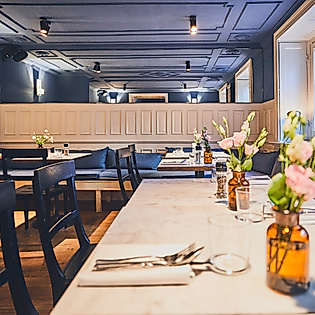 Elegant gedeckte Tische mit Blumen im Restaurant Cöllns Mutterland vor dunkelblauer Wandvertäfelung.