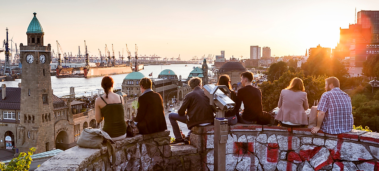 Menschen sitzen bei Sonnenuntergang oberhalb der Landungsbrücken mit Blick auf Hafen und Elbe