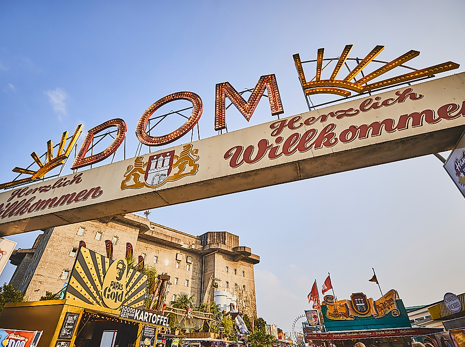 Eingangsportal des Hamburger DOM mit bunter Leuchtschrift und Fahrgeschäften im Hintergrund