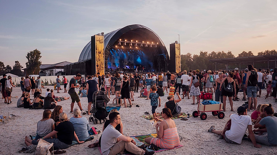 Publikum sitzt entspannt vor Open-Air-Bühne im Abendlicht