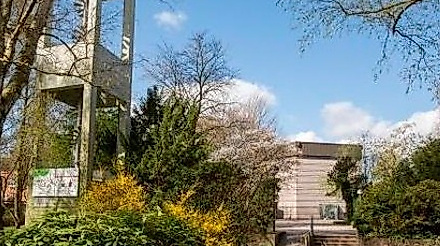 Kirchturm mit grünen Sträucher und im Hindergrund Kirchengebäude