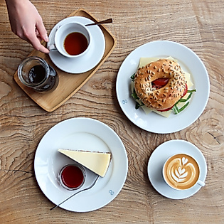 Frühstück mit Bagel, Käsekuchen, Cappuccino und Tee auf Holztisch im Café Elbgold, von oben fotografier