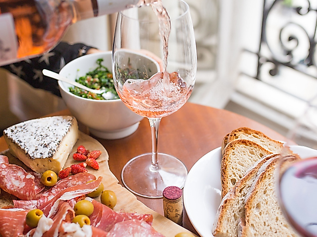 Französische Charcuterie-Platte mit Schinken, Käse, Oliven und Baguette, dazu Roséwein am Fenster.