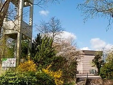 Kirchturm mit grünen Sträucher und im Hindergrund Kirchengebäude
