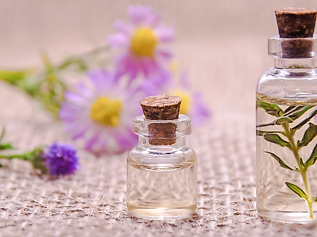 Zwei Fläschchen mit ätherischem Öl neben lila Blüten auf Leinenuntergrund