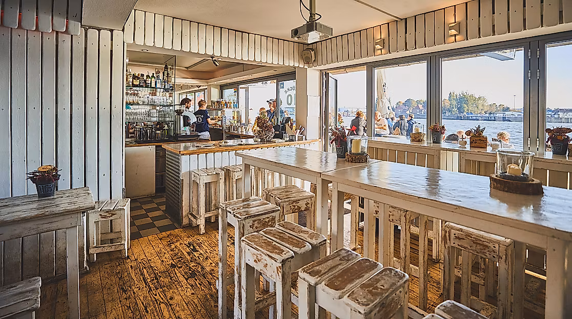 Helles Restaurant mit maritimem Interieur und Panoramablick auf den Hamburger Hafen durch große Fensterfront.