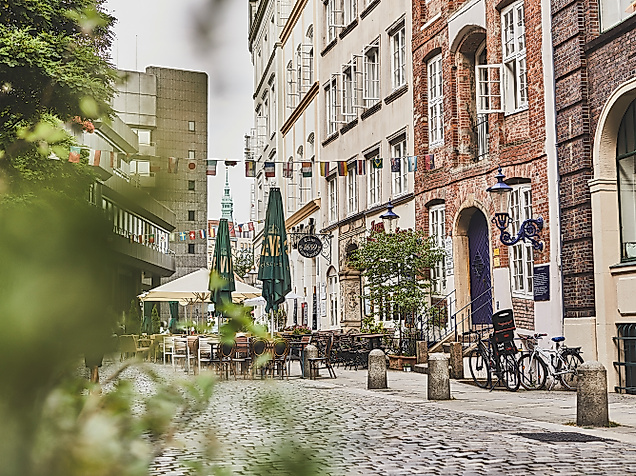 Pflasterstraße mit historischen Fassaden, Straßencafé und Begrünung in der Deichstraße Hamburg