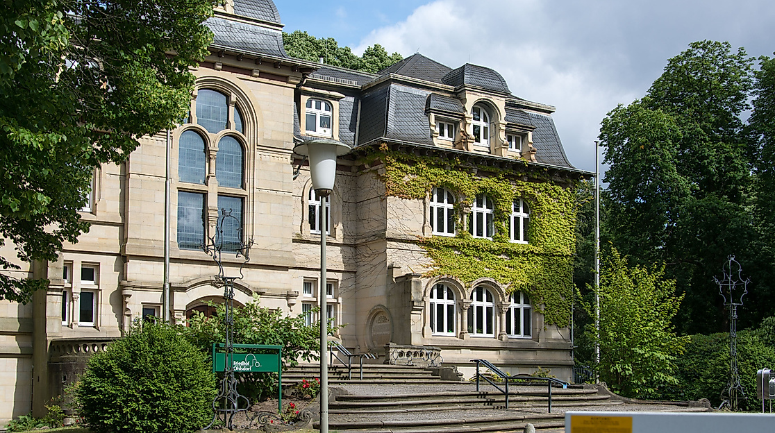 Historisches Verwaltungsgebäude auf dem Ohlsdorfer Friedhof, umgeben von Bäumen und Grünflächen.