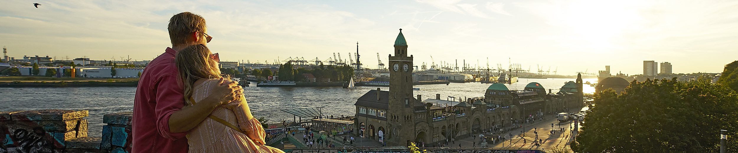 Ein Paar sitzt Arm in Arm auf dem Aussichtspunkt Stintfang. Im Hintergrund sind die Landungsbrücken.
