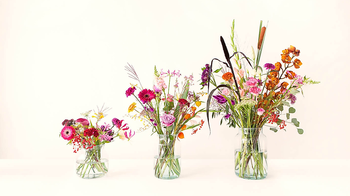 Drei unterschiedlich große Vasen mit bunt gemischten, kreativ arrangierten Blumen auf weißem Hintergrund