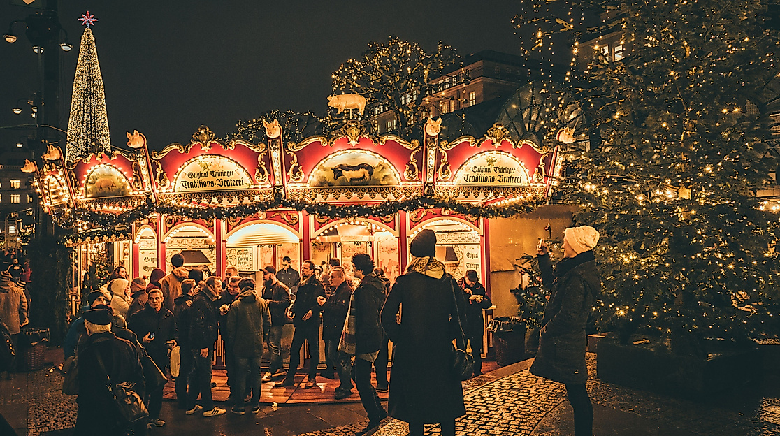 Visitors at a brightly lit Christmas market stall with carousel and Christmas tree in Hamburg at night
