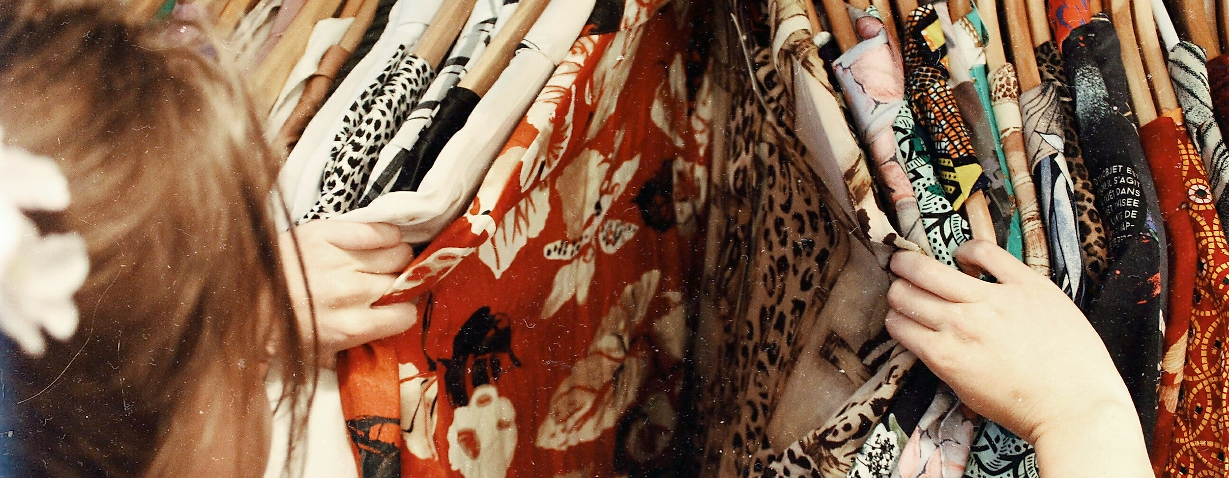 Personen stöbern durch bunt gemusterte Kleidungsstücke auf Holzkleiderbügeln in einem Hamburger Geschäft.