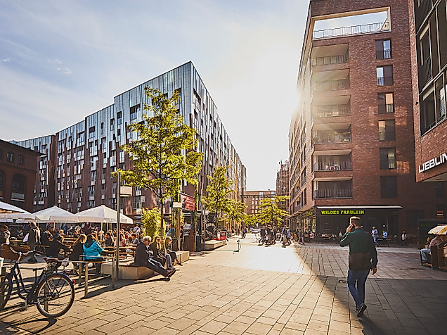 Sonniger Überseeboulevard in der HafenCity Hamburg mit Cafés, modernen Gebäuden und flanierenden Passant:innen