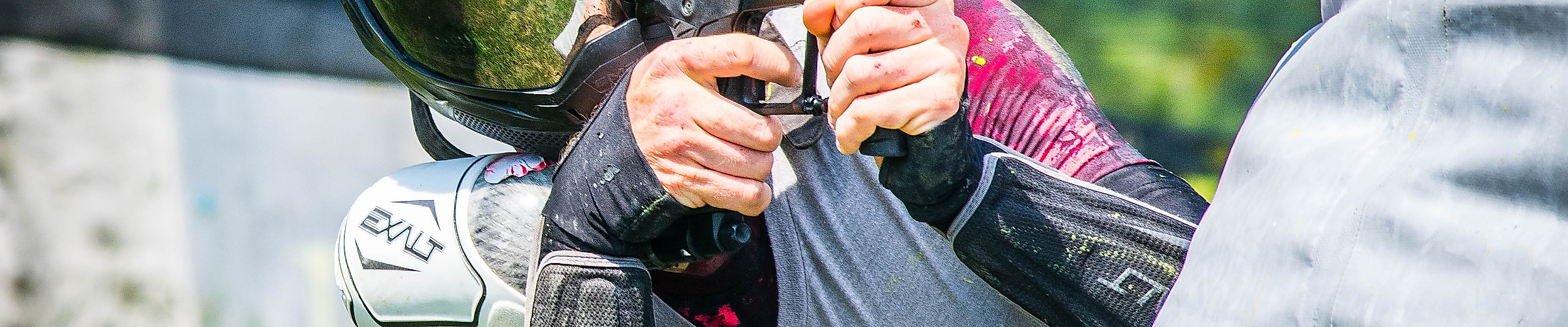Paintball-Spieler mit Schutzmaske und Markierer zielt konzentriert hinter einer Deckung im Spielfeld