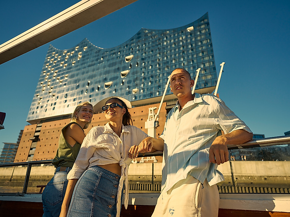 Three people on a boat in front of the Elbphilharmonie concert hall.