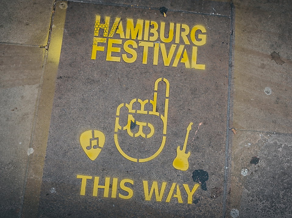Gelbes Straßenkunst-Logo „Hamburg Festival – This Way“ mit Hand- und Gitarrensymbol auf Asphalt