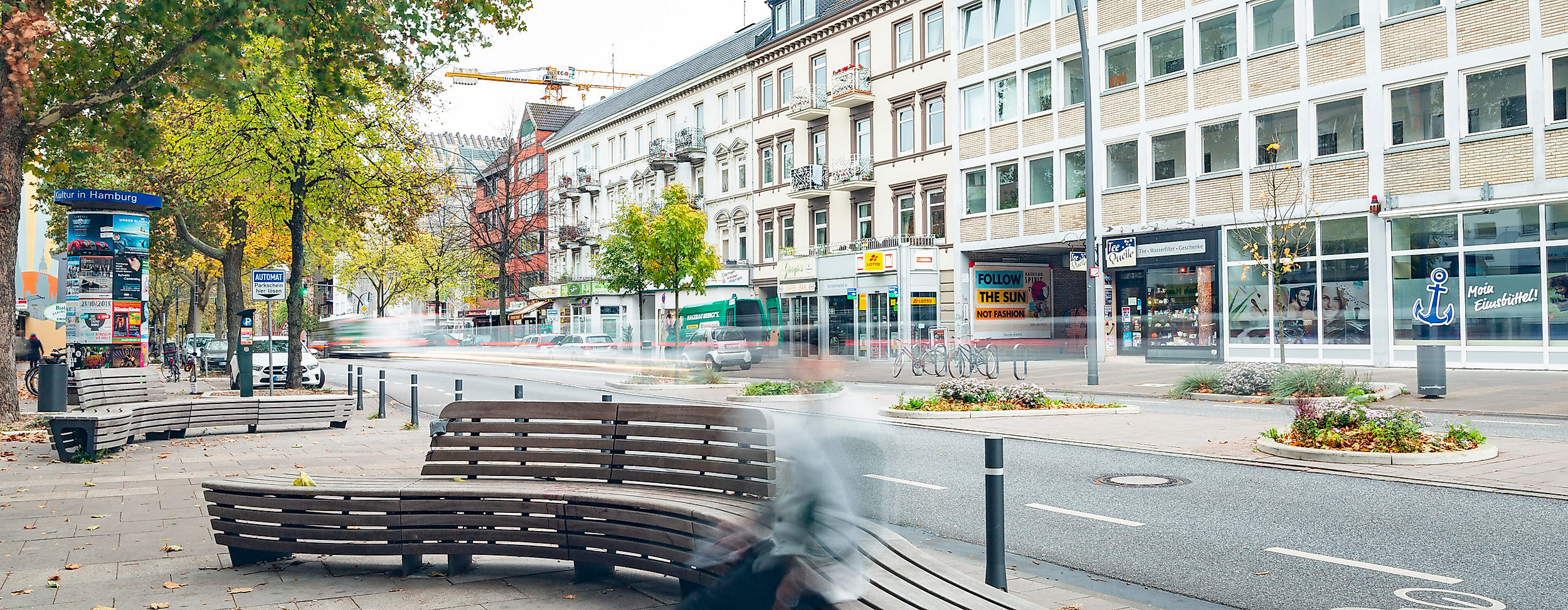 Fußgängerzone in Hamburg-Eimsbüttel mit modernen Holzbänken, Geschäften und herbstlich gefärbten Bäumen