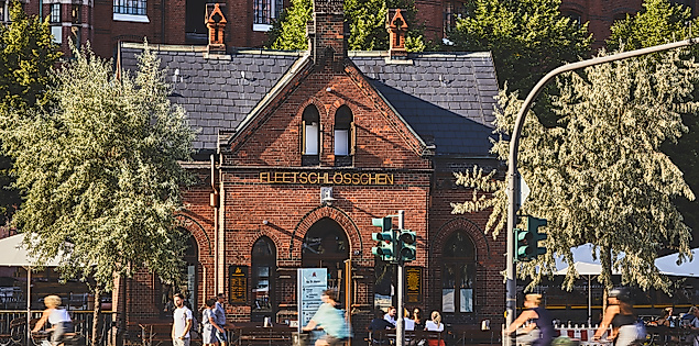 Backsteinhaus Fleetschlösschen in der Speicherstadt, umgeben von Bäumen und Passant:innen