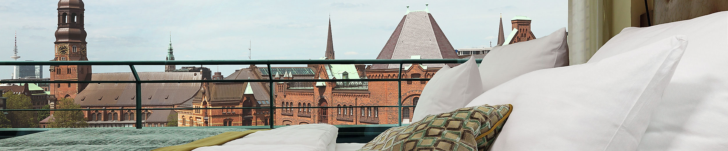 Blick vom Hotelbett Ameron Hotel Speicherstadt Hamburg auf Hamburgs Speicherstadt mit Kirchtürmen und moderner Architektur im Hintergrund.