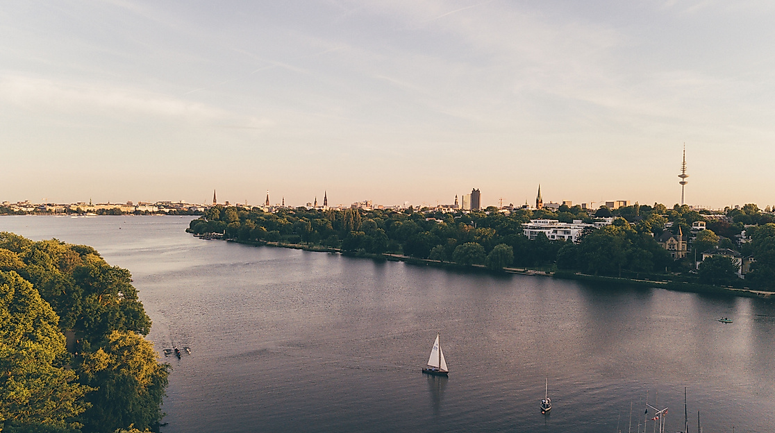 Luftaufnahme der Außenalster mit Segelbooten und Blick auf Hamburgs Skyline im Abendlicht.