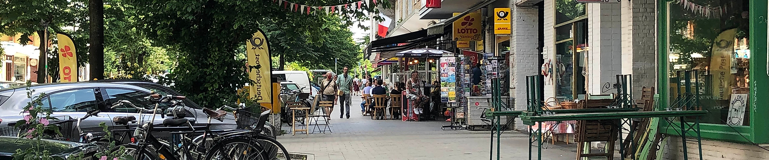 Straßenszene an der Weidenallee in Hamburg mit Cafés, kleinen Läden und abgestellten Fahrrädern im Schatten