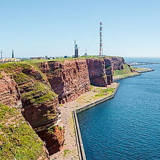 Rote Felsen von Helgoland mit Leuchtturm und blauem Meer unter klarem Himmel