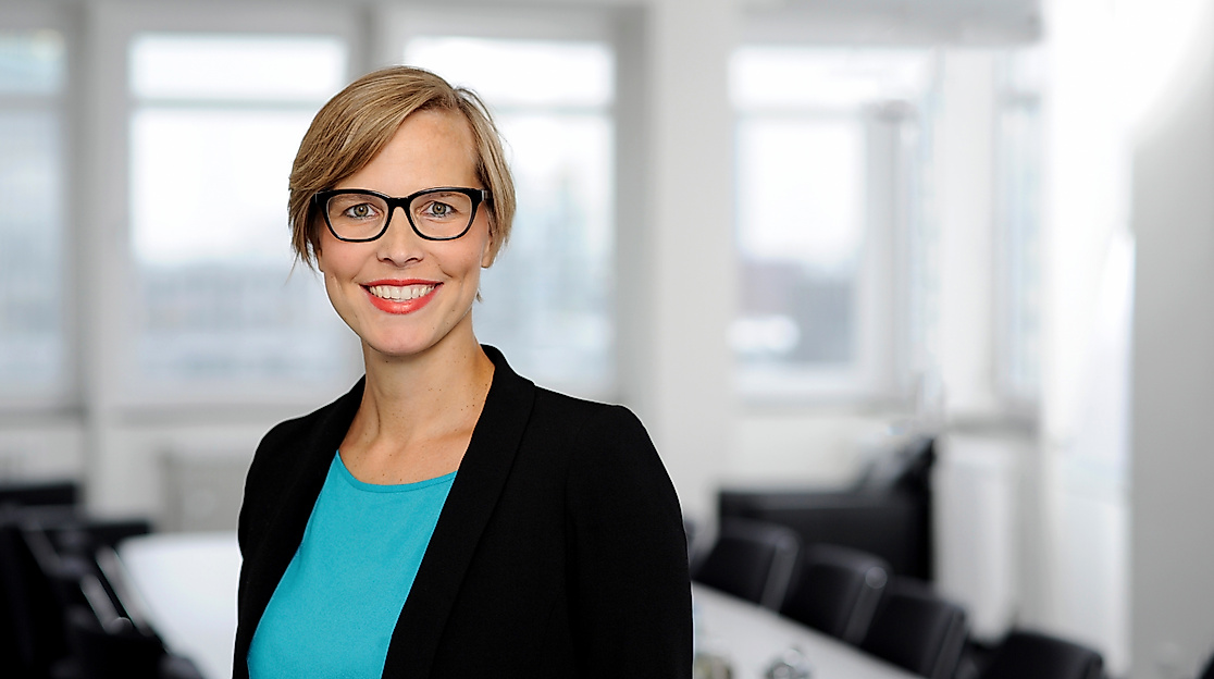 Porträt einer Frau mit Brille im schwarzen Blazer und türkisfarbenem Oberteil vor hellem Konferenzraum, Ansprechpartnerin der Hamburg Tourismus GmbH