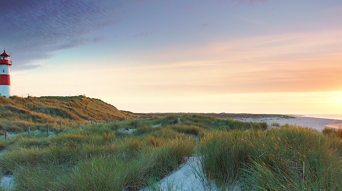 Panoramablick auf Sylt mit Leuchtturm in den Dünen und Sonnenuntergang über der Nordsee