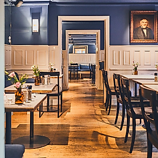 Stilvoller Innenraum des Restaurants Cöllns Mutterland mit dunklen Holzmöbeln und klassischem Wandporträt