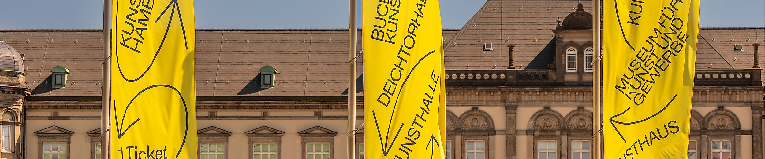 Gelbe Kunstmeile-Fahnen vor klassizistischer Fassade am Hamburger Glockengießerwall bei blauem Himmel