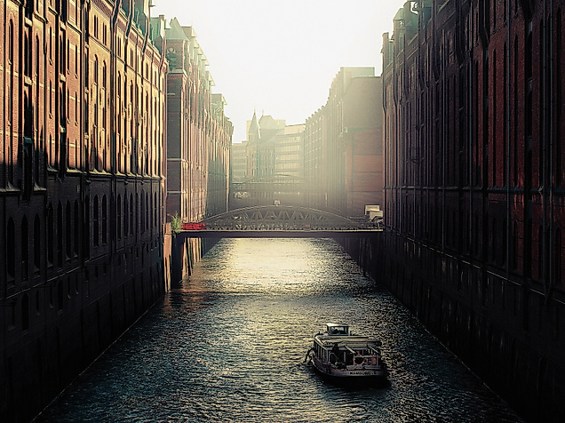 Schmale Wasserstraße der Speicherstadt im Gegenlicht mit reflektierendem Wasser und Backsteinfassaden