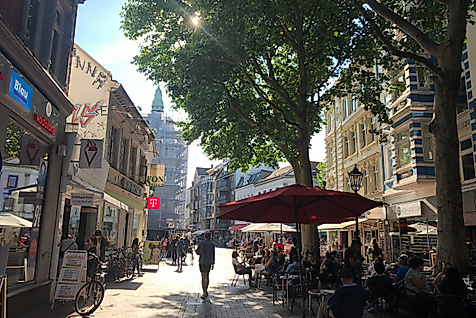 Belebte Ottensener Hauptstraße in Hamburg mit Geschäften, Straßencafés und Passant:innen im Sonnenlicht