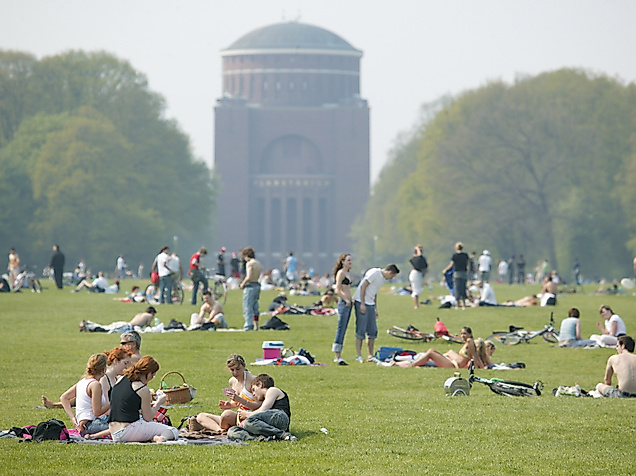 Zahlreiche Menschen entspannen auf der großen Wiese im Stadtpark mit Blick auf das Planetarium Hamburg