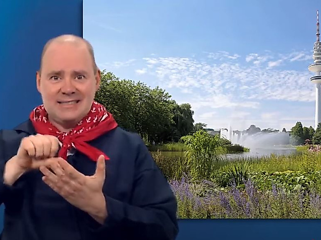 Mann gebärdet vor Hamburg-Kulisse mit Parklandschaft und Fernsehturm – barrierefreie Infos zu Grünflächen.
