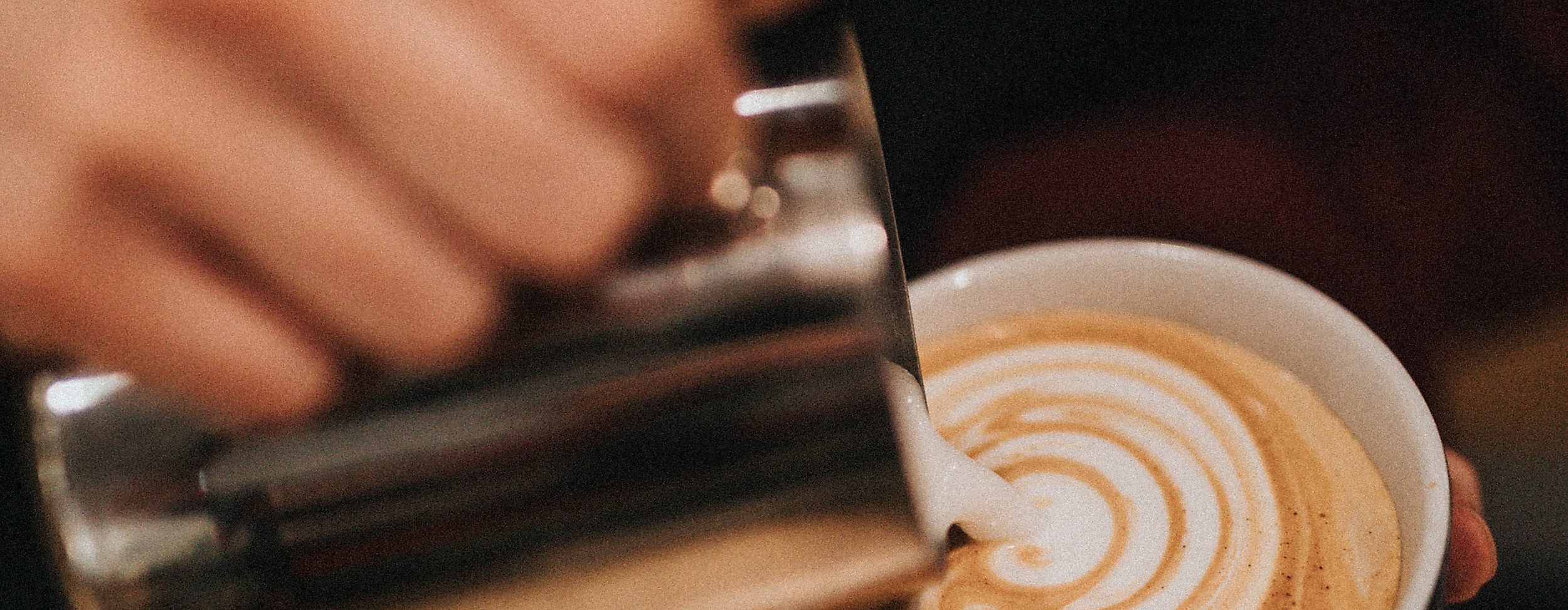 Barista gießt kunstvoll Milchschaum in Cappuccino und kreiert Latte-Art im Café in Hamburg