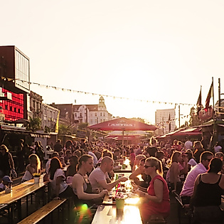 Menschenmenge bei Sonnenuntergang auf dem Spielbudenplatz, gesäumt von Bars, Lichtern und Open-Air-Sitzplätzen