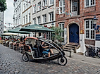 Rikscha fährt durch enge Altstadtgasse mit Außengastronomie und historischen Fassaden in Hamburg