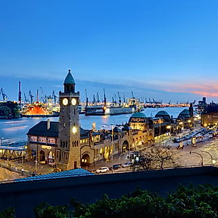 Abendstimmung an den Hamburger Landungsbrücken mit Blick auf Elbe, Hafen und beleuchtete Schiffe.