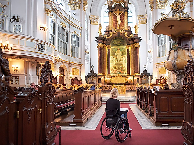 Rollstuhlnutzerin mit Assistenzhund im barrierefrei zugänglichen Kirchenschiff des Hamburger Michel.