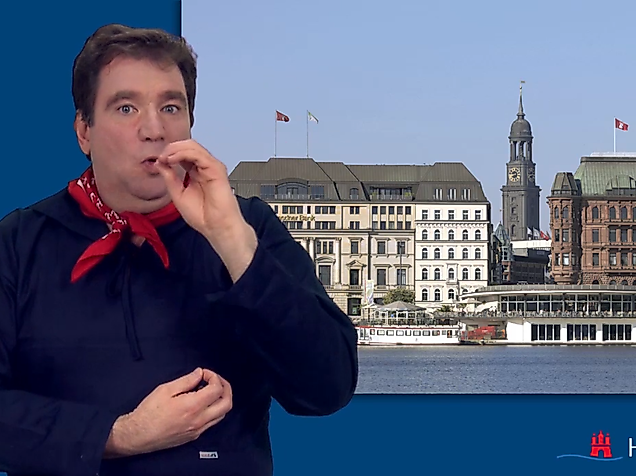 Man signing in International Sign in front of Hamburg’s inner city with Alster arcades and city hall tower.